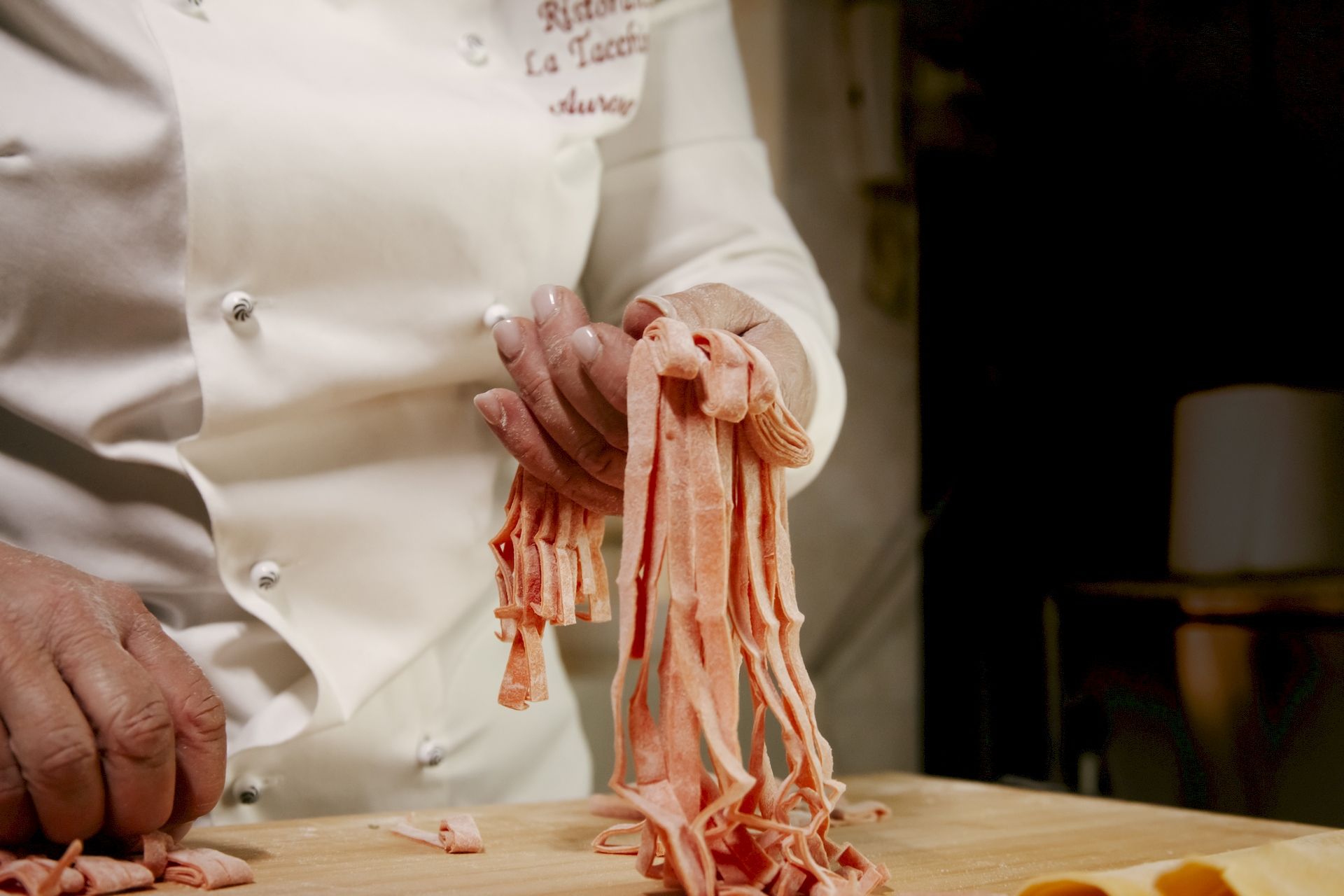 Aurora chef prende in mano fettuccine arancio durante preparazione piatto Tricolore fettuccine all'uovo di spinaci con funghi e tartufo del Ristorante La Tacchinella di Canzano a Teramo in Abruzzo